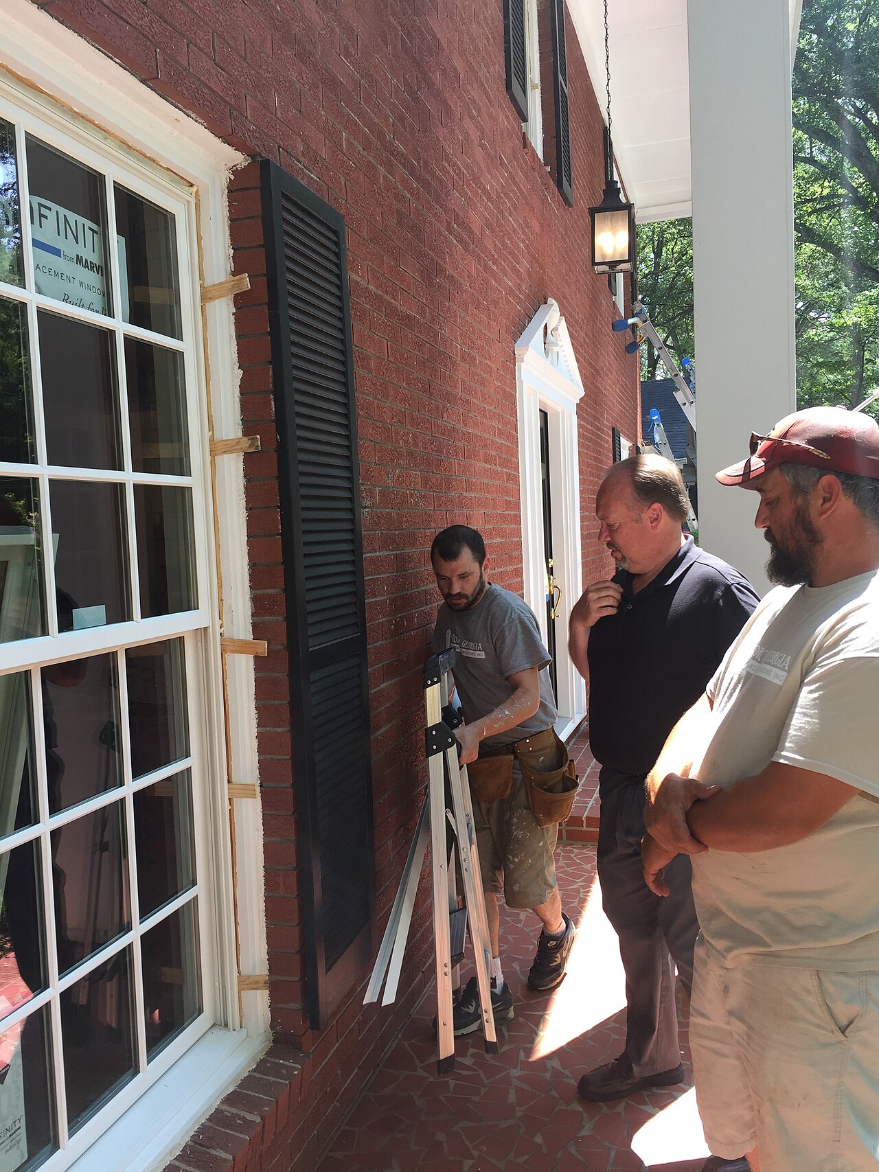 Workers inspecting a residential fiberglass window installation on a brick home