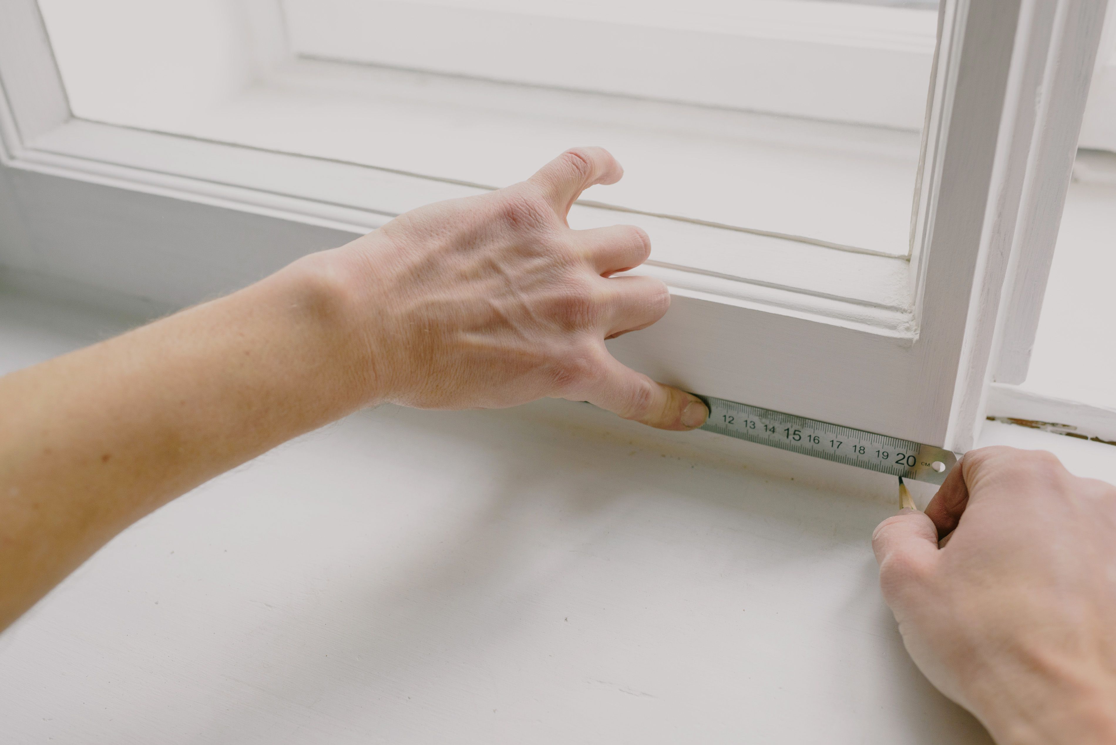 Hands measuring a window frame before replacement